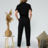 Young woman with blond hair wearing black organic cotton 7/8 length short sleeve jumpsuit with side pockets and coconut buttons