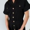 Young woman with blond hair wearing black organic cotton 7/8 length short sleeve jumpsuit with side pockets and coconut buttons