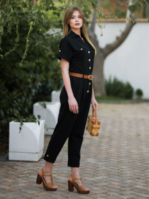 Young woman with blond hair wearing black organic cotton 7/8 length short sleeve jumpsuit with side pockets and coconut buttons