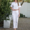 Young woman with blond hair wearing white organic cotton white 7/8 length short sleeve jumpsuit with side pockets and coconut buttons