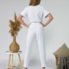 Young woman with blond hair wearing white organic cotton white 7/8 length short sleeve jumpsuit with side pockets and coconut buttons