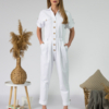 Young woman with blond hair wearing white organic cotton white 7/8 length short sleeve jumpsuit with side pockets and coconut buttons