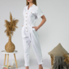 Young woman with blond hair wearing white organic cotton white 7/8 length short sleeve jumpsuit with side pockets and coconut buttons