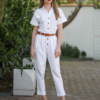 Young woman with blond hair wearing white organic cotton white 7/8 length short sleeve jumpsuit with side pockets and coconut buttons