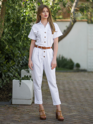 Young woman with blond hair wearing white organic cotton white 7/8 length short sleeve jumpsuit with side pockets and coconut buttons