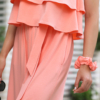 A woman wearing a peach color two-piece outfit and white sandals. She is near a covered seating area with floral cushions and greenery in the background.