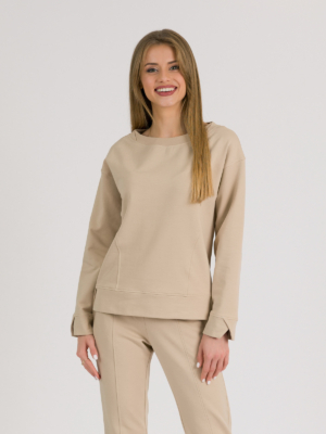 woman with blond hair wearing beige organic cotton long sleeve off shoulder boat neck blouse and beige organic cotton long tapered leg pants
