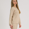 woman with blond hair wearing beige organic cotton long sleeve off shoulder boat neck blouse and beige organic cotton long tapered leg pants