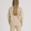 woman with blond hair wearing beige organic cotton long sleeve off shoulder boat neck blouse and beige organic cotton long tapered leg pants