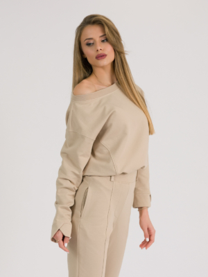 woman with blond hair wearing beige organic cotton long sleeve off shoulder boat neck blouse and beige organic cotton long tapered leg pants