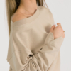 woman with blond hair wearing beige organic cotton long sleeve off shoulder boat neck blouse and beige organic cotton long tapered leg pants