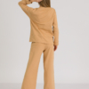 woman with blond hair wearing brown organic cotton long sleeve off shoulder boat neck blouse and brown organic cotton long wide legs pants