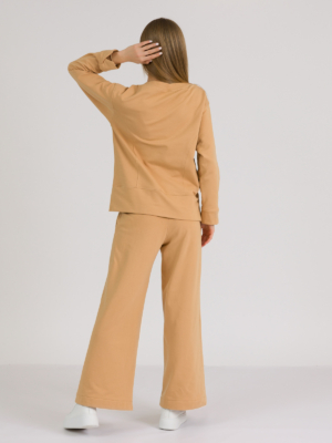 woman with blond hair wearing brown organic cotton long sleeve off shoulder boat neck blouse and brown organic cotton long wide legs pants