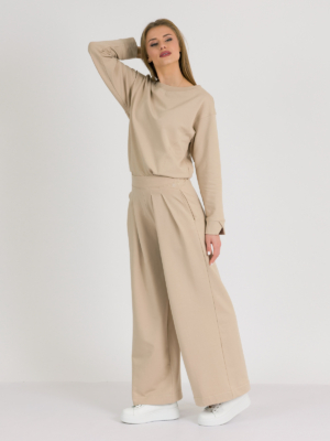 Woman with blond hair wearing beige organic cotton blouse and beige long wide pants