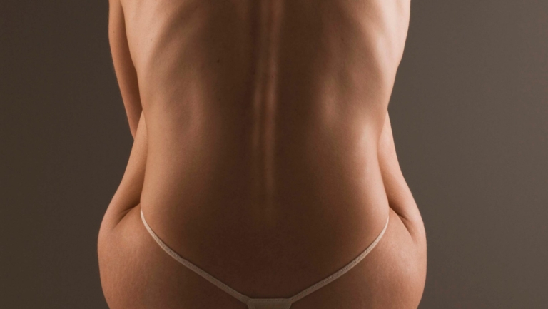 A close-up of a person's bare back and sides, showcasing the natural curves and skin tones, wearing minimal white thong underwear.