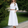 Woman wearing white organic cotton shirt dress with bracelet sleeves coconut buttons and waist belt