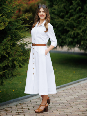 Woman wearing white organic cotton shirt dress with bracelet sleeves coconut buttons and waist belt