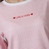 Woman wearing white organic cotton pants and pink striped organic cotton t-shirt with embroidery "Less is more"