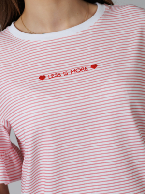 Woman wearing white organic cotton pants and pink striped organic cotton t-shirt with embroidery "Less is more"