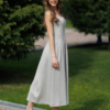 Woman wearing gray organic cotton dress with a flared skirt, midi length, square neckline, high waist and pockets.
