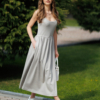 Woman wearing gray organic cotton dress with a flared skirt, midi length, square neckline, high waist and pockets.