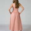 Woman wearing pink organic cotton dress with a flared skirt, midi length, square neckline, high waist and pockets.