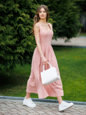 Woman wearing pink organic cotton dress with a flared skirt, midi length, square neckline, high waist and pockets.