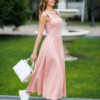 Woman wearing pink organic cotton dress with a flared skirt, midi length, square neckline, high waist and pockets.