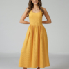Woman wearing yellow organic cotton dress with a flared skirt, midi length, square neckline, high waist and pockets.