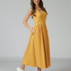 Woman wearing yellow organic cotton dress with a flared skirt, midi length, square neckline, high waist and pockets.