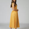 Woman wearing yellow organic cotton dress with a flared skirt, midi length, square neckline, high waist and pockets.