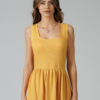 Woman wearing yellow organic cotton dress with a flared skirt, midi length, square neckline, high waist and pockets.