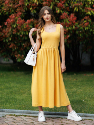 Woman wearing yellow organic cotton dress with a flared skirt, midi length, square neckline, high waist and pockets.