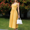 Woman wearing yellow organic cotton dress with a flared skirt, midi length, square neckline, high waist and pockets.