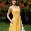 Woman wearing yellow organic cotton dress with a flared skirt, midi length, square neckline, high waist and pockets.