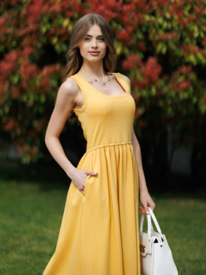 Woman wearing yellow organic cotton dress with a flared skirt, midi length, square neckline, high waist and pockets.