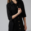 Woman wearing black organic cotton shirt dress with bracelet sleeves coconut buttons and waist belt