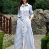 Dark-haired woman wearing a long blue striped linen dress with coconut buttons and collar