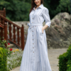 Dark-haired woman wearing a long blue striped linen dress with coconut buttons and collar