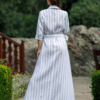 Dark-haired woman wearing a long blue striped linen dress with coconut buttons and collar