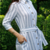 Dark-haired woman wearing a long blue striped linen dress with coconut buttons and collar