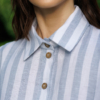 Dark-haired woman wearing a long blue striped linen dress with coconut buttons and collar