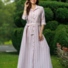 Dark-haired woman wearing a long pink striped linen dress with coconut buttons and collar