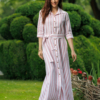 Dark-haired woman wearing a long pink striped linen dress with coconut buttons and collar