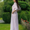 Dark-haired woman wearing a long pink striped linen dress with coconut buttons and collar