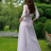 Dark-haired woman wearing a long pink striped linen dress with coconut buttons and collar
