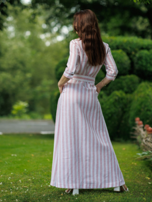Dark-haired woman wearing a long pink striped linen dress with coconut buttons and collar