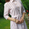 Dark-haired woman wearing a long pink striped linen dress with coconut buttons and collar