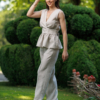A dark-haired woman wearing a beige elegant top with a belt at the waist, a V-neckline and an open back, and beige pants made of 100% linen.