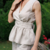 A dark-haired woman wearing a beige elegant top with a belt at the waist, a V-neckline and an open back, and beige pants made of 100% linen.